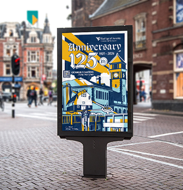 Potomac State Poster made for their 125th anniversary photographed in context, on a busy street the primary colors are light blue, dark blue, gold, and white